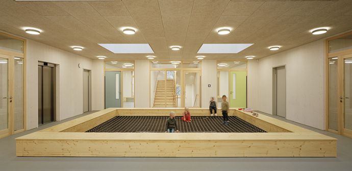 Holz-Modul-Bau Kita Worther Weg Kinder auf einer Art Trampolin innerhalb eines Gebäudes aus Holz